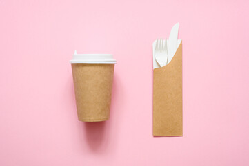 Paper cup for coffee and disposable fork with a knife in a cardboard case on a pink background