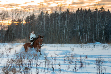 A girl in a white cloak rides a brown horse in winter.