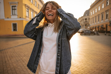 Mad caucasian young girl ruffled her hair with hands while laughing in open area. Snow-white smile on face of tanned blonde. People sincere emotions lifestyle concept.