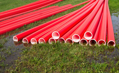 Bright red plastic water pipes on a wet green lawn are prepared for the installation of a water main.	
