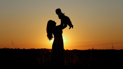 Unrecognizable family silhouette at sunset, happy mother throws up her baby, motherly love