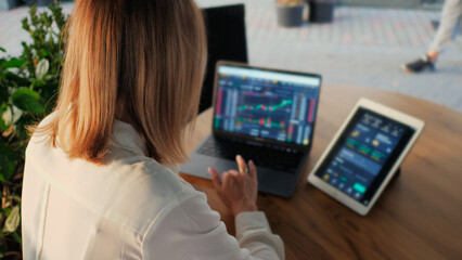 Unrecognizable woman trader trades and analyzes the cryptocurrency market, invests money while sitting in a cafe, use laptop