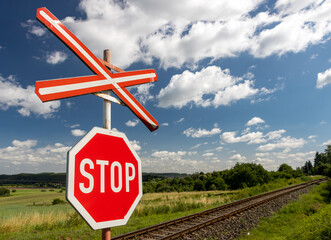 A red STOP sign before crossing the tracks.