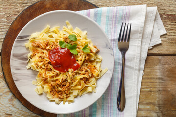 Bolognese pasta garnished with herbs and cheese in a plate on a round stand next to a fork and a napkin.