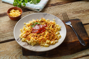 Pasta bolognese garnished with herbs and cheese in a plate on a wooden table on a stand next to a fork.