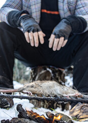 The homeless man grills a rat, in a snowy landscape, close up view.