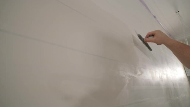 Man plastering the walls with finishing putty in room with putty spatula