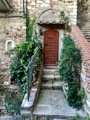 Italian house. Fragment of facade. Wooden door. Stone wall, medieval building in Umbria or Tuscany. Plant in pot. Housr covered Ivy.