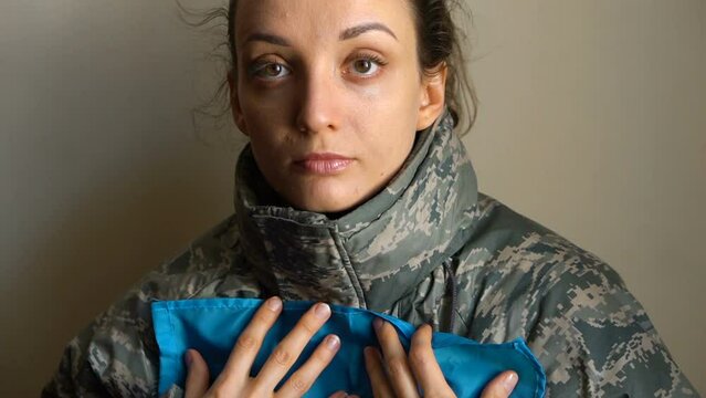 Young female soldier is holding ukrainian flag with love and anxiety due to escalation military conflict on the western part of Ukraine, Russian invasion, war concept