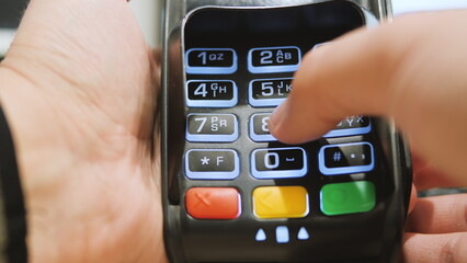 Payment terminal. A man enters a PIN code. Close up of a hand on a credit card pin pad at a retail...
