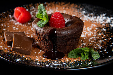 Small chocolate cake filled with liquid chocolate. Traditional French dessert coulant. Tasty hot cake melting chocolate syrup and decorated with cocoa powder, raspberries and mint.