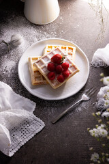 Homemade waffles with strawberries, raspberries and powdered sugar on white dish. Top view