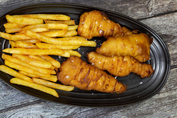 Battered chicken fillets with french fries, seasoned with sea salt, on a black stoneware plate.  On a wooden background