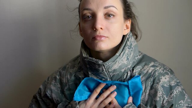Young female soldier is holding ukrainian flag with love and anxiety due to escalation military conflict on the western part of Ukraine, Russian invasion, war concept