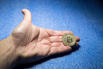 Male hand holding a golden bitcoin isolated on blue background. Cryptocurrency, investment, savings, trading and financial market concept.	
