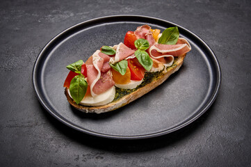 Close up bruschetta with mozzarella, Parma ham and pesto on black plate on graphite background