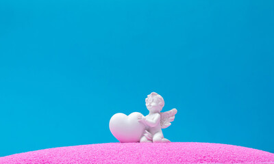 Angel with heart on pink sand and blue background. Minimal background concept. Love is in the air.