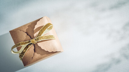 Kraft paper gift box with golden ribbon bow on white with shadows