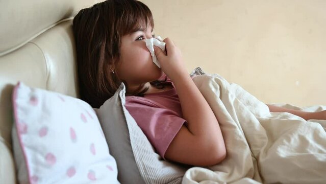 a 10-year-old girl lies in bed sick, coughs, blows her nose into a napkin. High quality 4k footage