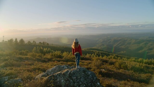 Travel blogger, adventure explorer reach the top of mountain hill at sunset. Young woman in red sweater stand on top of beautiful mountain top. Cinematic social media influencer