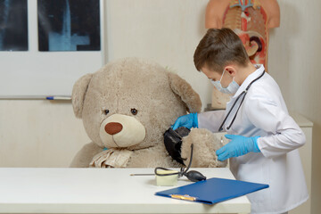 a boy in a doctor's suit measures the pressure of a teddy bear