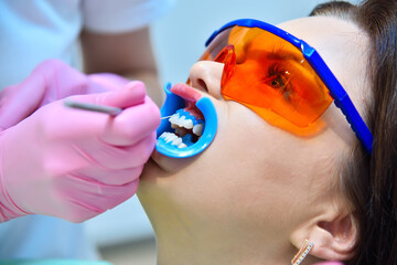 Woman dentist prepares woman patient for teeth whitening procedure.