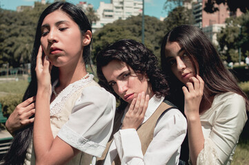 three pretty young girls standing in a park posing touching their faces.
