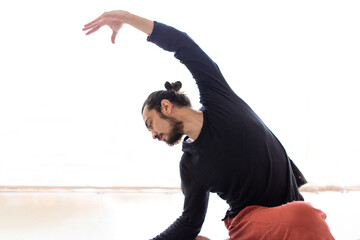 Young Caucasian long haired white man is performing yoga in a studio or house.