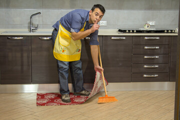 boy doing housework while making a gesture of silence and hiding dirt under the carpet