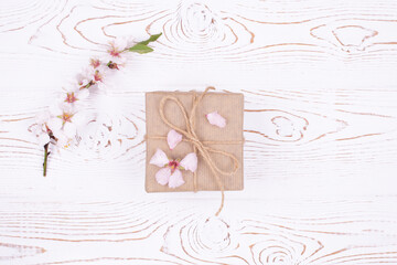 Spring composition gift in the center, wrapped in craft paper, spring blossoming almond branch with flowers on a gray whitewashed rustic wooden table. Flat lay, copy space