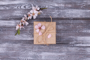 Spring composition gift in the center, wrapped in craft paper, spring blossoming almond branch with flowers on a gray whitewashed rustic wooden table. Flat lay, copy space