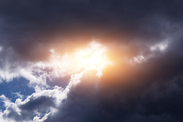 Dark storm cumulus clouds with yellow orange bright sun and sunlight, sky background