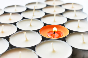 A close up image of a single lit orange tea light candle with several white tea light candles. 