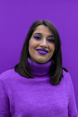 vertical portrait of a happy young woman smiling looking at the camera dressed and made up in purple on purple background