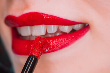 Glossy passionate red lips. Woman applying liquid lipstick or gloss. Shiny smile. Lady with natural...