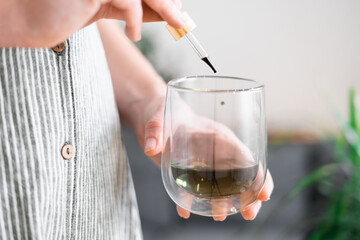 Woman hand holding dropper with green chlorophyll at home. Immunity booster concept 