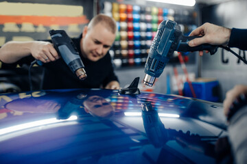 Car wrapping specialists putting vinyl foil or film on car. Selective focus.