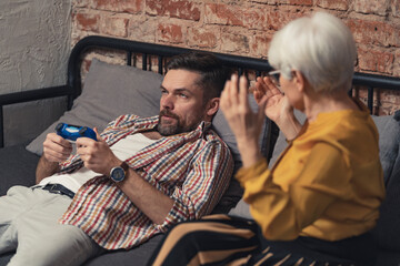quarrel between grandmother and her lazy middle-aged son does nothing but play games. High quality photo - obrazy, fototapety, plakaty