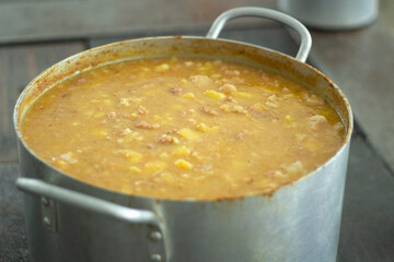 Soup in saucepan. Large container with pea soup in kitchen. Stainless steel cookware. Steel tank with food in dining room.