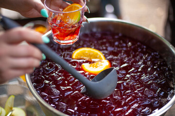 Punch at party. Cocktail with alcohol. Girl pours drink into glass. Details of holiday on street. Treat for everyone.