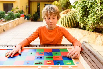 Student boy using a montessori checker board outdoors doing homeschooling.