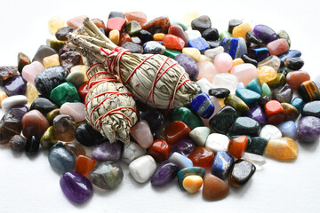 A low angle image of two white sage smudge sticks with a variety of polished healing crystals. 