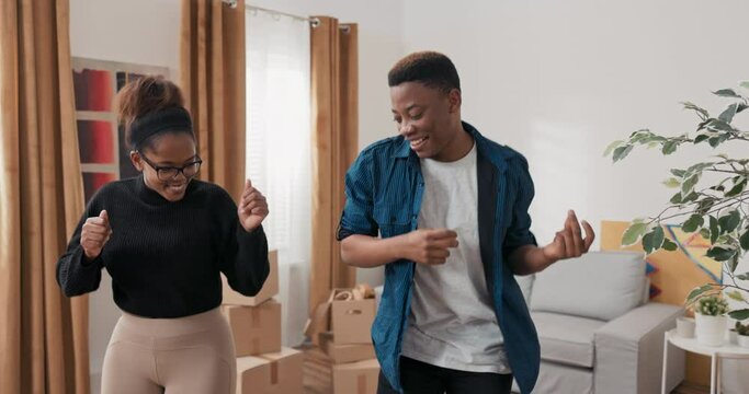 A couple in love moves into a new apartment, the removal of all the cardboard boxes, a new chapter in life, buying, renting a house, the boy along with the girl dance with joy, hugging, high-five