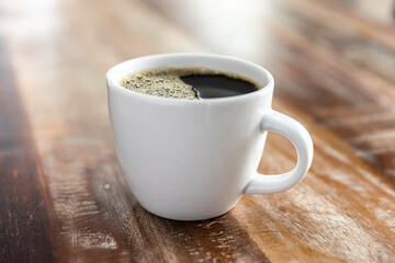 Cup of black coffee in a white mug on a wood table.
