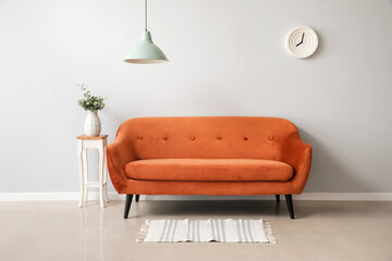 Stylish brown sofa and table with vase near light wall