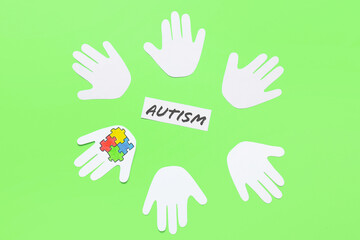 Paper human palms with colorful puzzle pieces and word AUTISM on color background