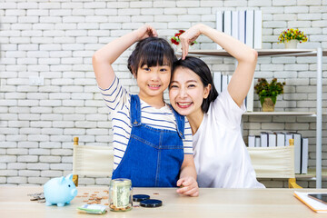 Fototapeta premium Asian mother is teaching her daughter the saving lesson for investment in education and future planning whiile posing with heart gesture