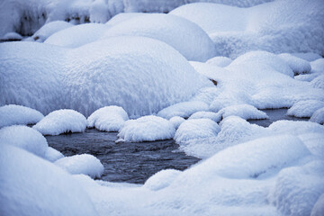 Stones with snow caps and ice in the water of frozen river in winter.