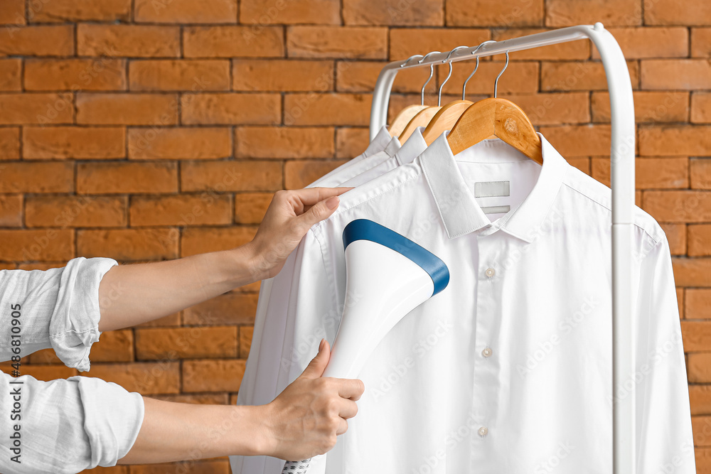 Wall mural Woman ironing shirts with steam near brick wall