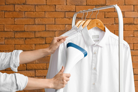 Woman ironing shirts with steam near brick wall